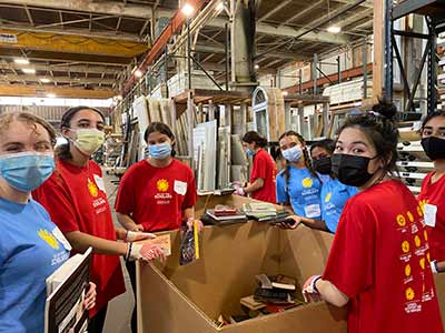 Masked college students smile at the camera while working in a warehouse